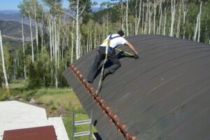 Man walking along sloped roof tethered to the snow guard for safety
